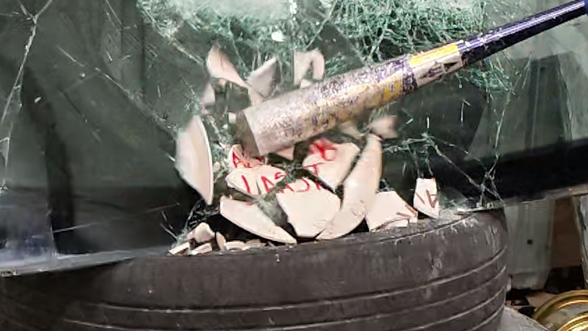 A bat strikes the “Always Last” plate on a tire, sending pieces into the air.