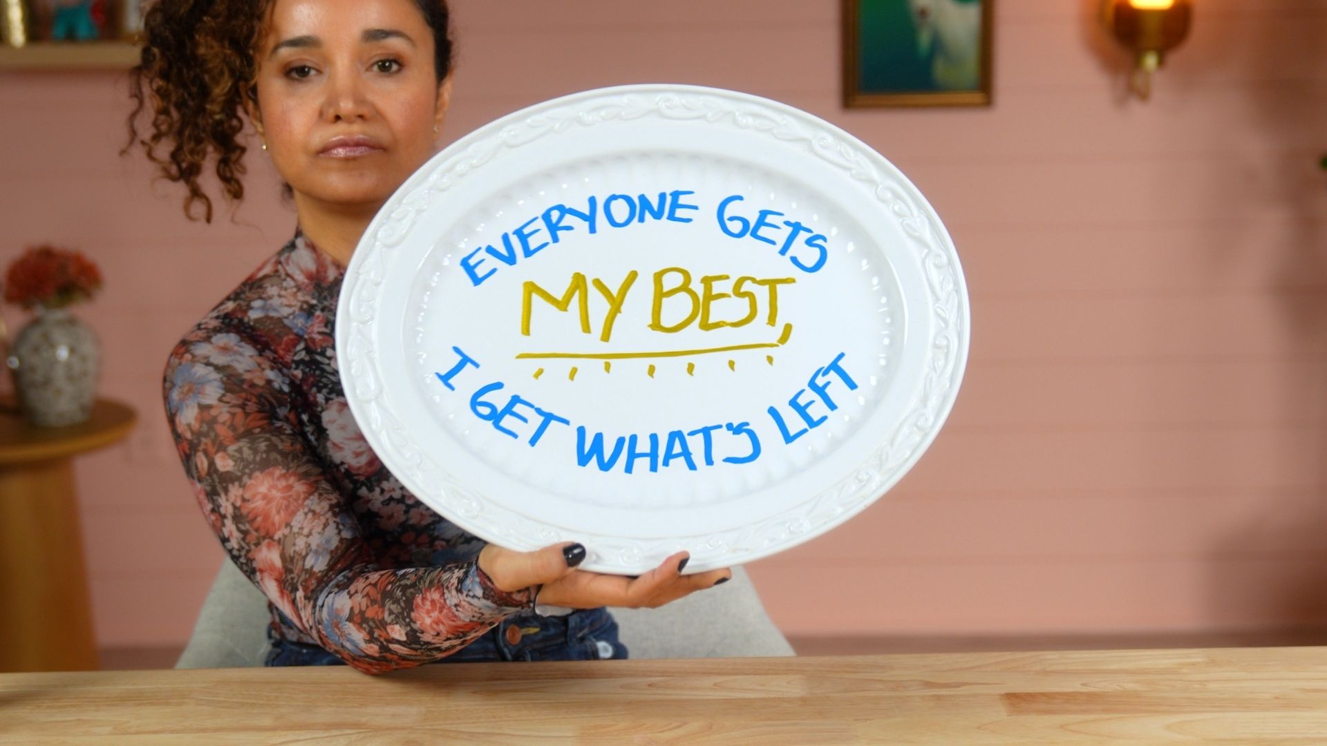 Veronica holds a serving platter reading “Everyone gets my best. I get what’s left,” written in blue and yellow.