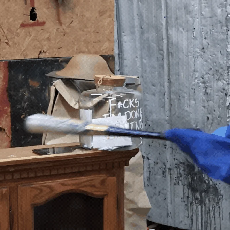 A bat hits the glass jar labeled “F*cks I’m done giving” in the rage room.