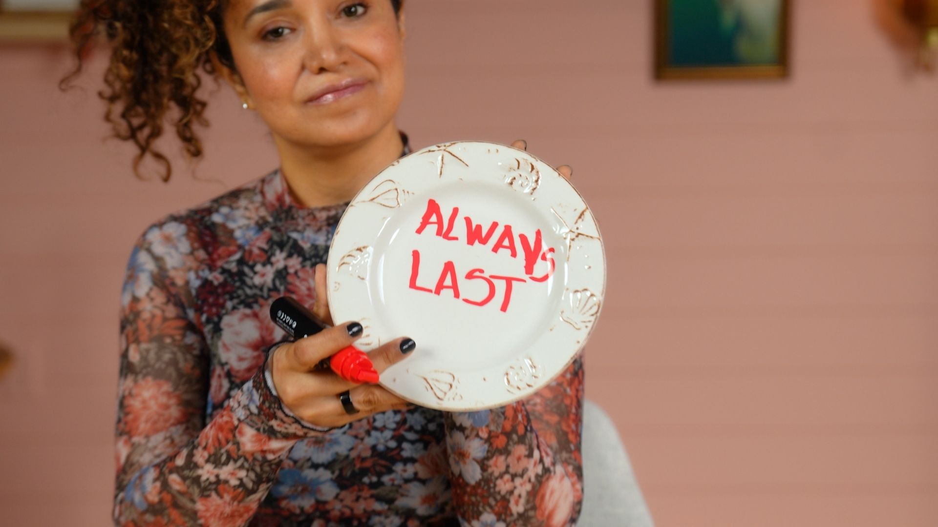 Veronica holds a floral plate with “Always Last” handwritten in red.