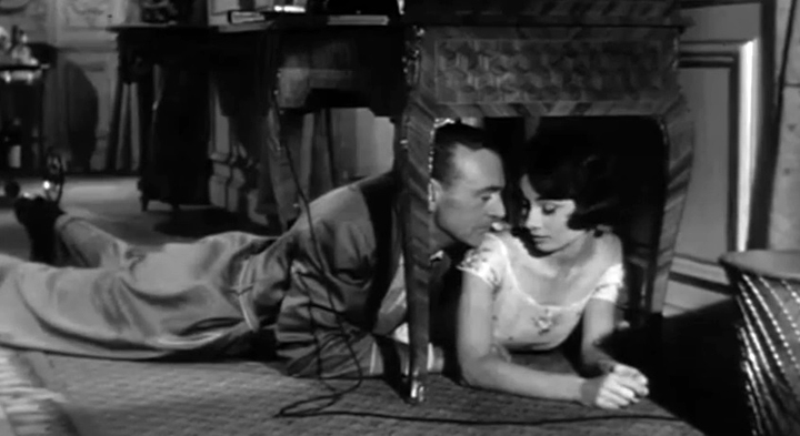 Gary Cooper and Audrey Hepburn lying beside one another beneath a table in the 1957 Love in the Afternoon trailer.